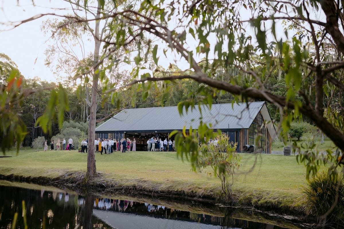 The glass-gabled barn beside the dam, guests gathered on the lawn
